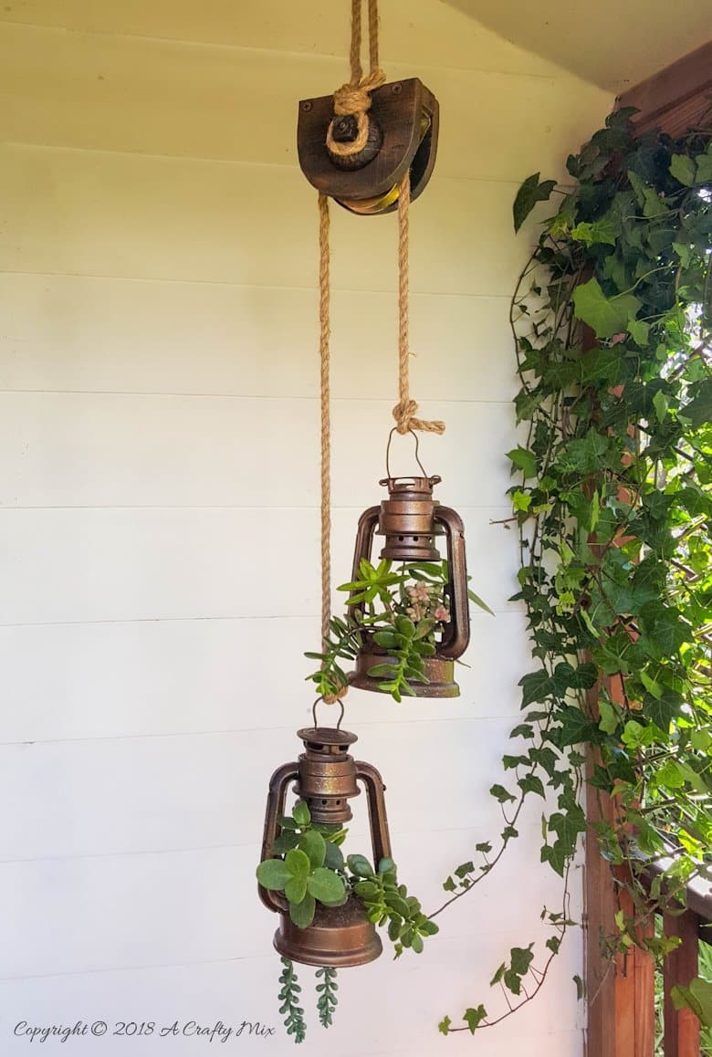 A faux wooden pulley and two old lantern planters hanging on a porch