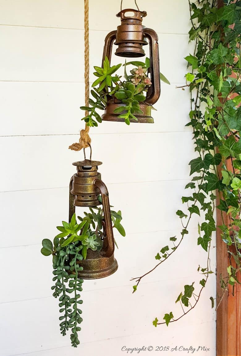 Charming old school lantern planters filled with succulents hanging on a porch. 