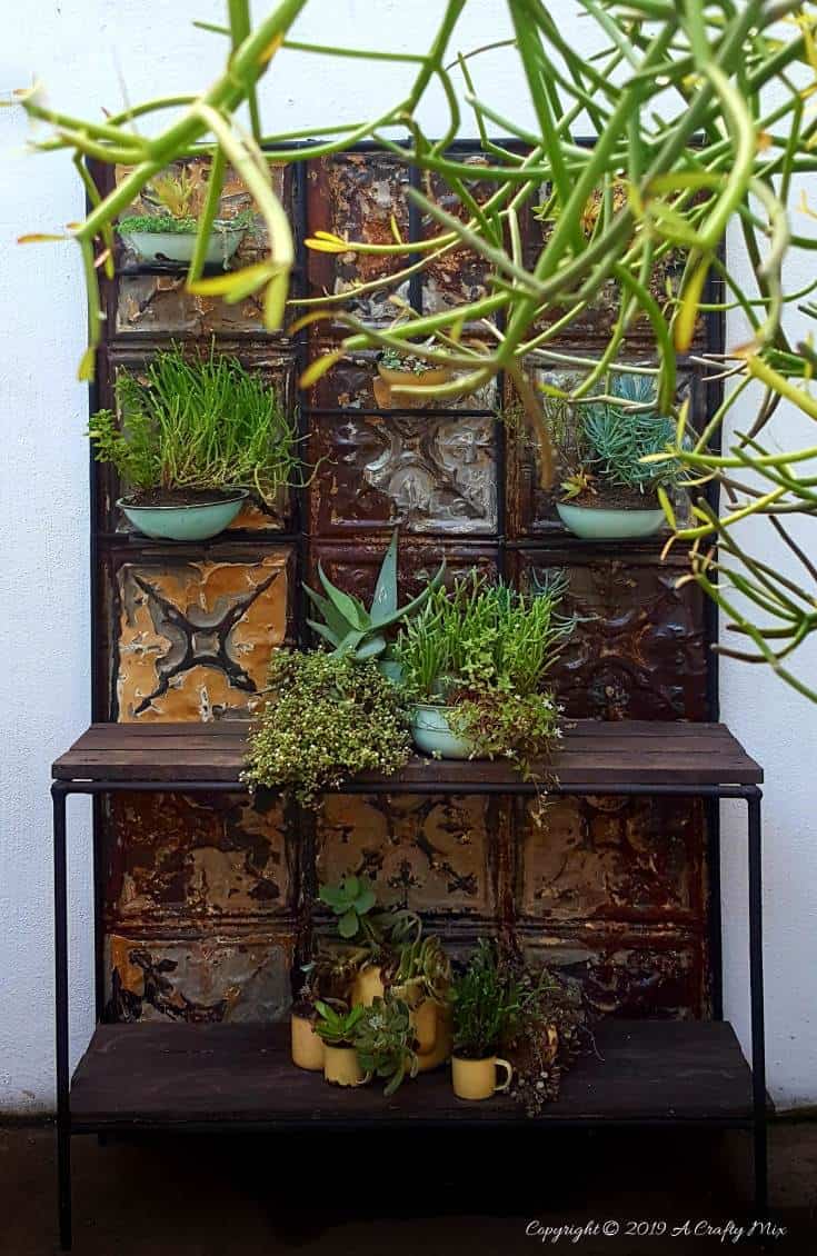 How to makeover an old plant stand using ceiling rusty tin ceiling tiles. Includes 3 ways to clean and prepare the tiles for craft projects #tinceilingideas #tinceilinghomedecor #tinceilingtilesrepurposed #plantstandideas #ACraftyMix