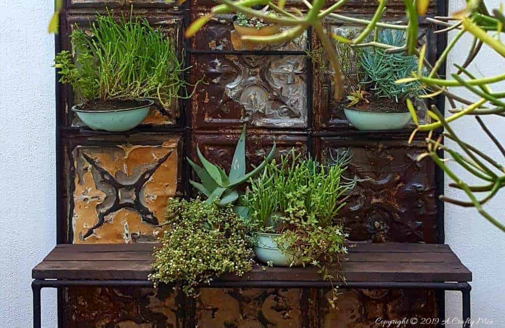 How to makeover an old plant stand using ceiling rusty tin ceiling tiles. Includes 3 ways to clean and prepare the tiles for craft projects #tinceilingideas #tinceilinghomedecor #tinceilingtilesrepurposed #plantstandideas #ACraftyMix