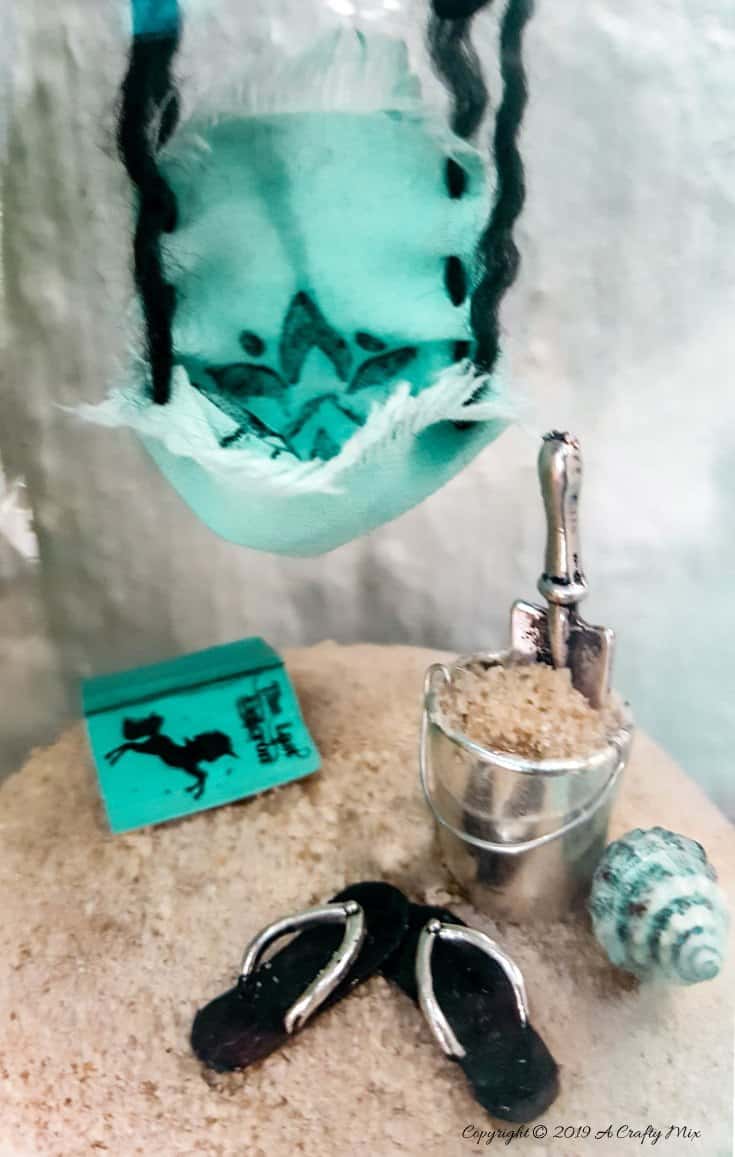How to recycle a broken wine glass and make a fairy beach in a cloche #FairyGarden #FairyGardenIdeas #ACraftyMix #FairyGardenDIY #FairyBeachDIY #FairyGardenDesigns #ClocheDecor #ClocheIdeas #WineGlassCloche #ClocheDIY #WineGlassRepurpose #UnicornSPiT
