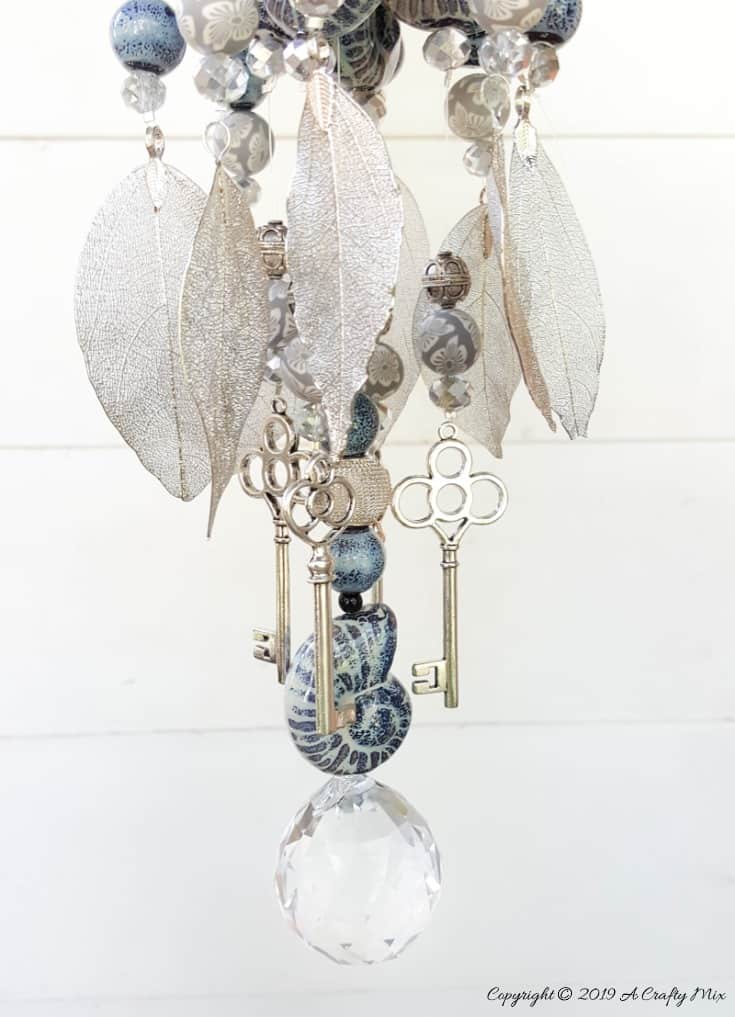 A close up of the delicate silver leaves and keys on the upcycled denim wind chime #DIYDenim #DenimIdeas #DenimMobile #DenimUpcycleIdeas #ACraftyMix #DenimUpcycle #DIYWindChime #TinCanRecycle #TinCanMobile #DenimWindChime