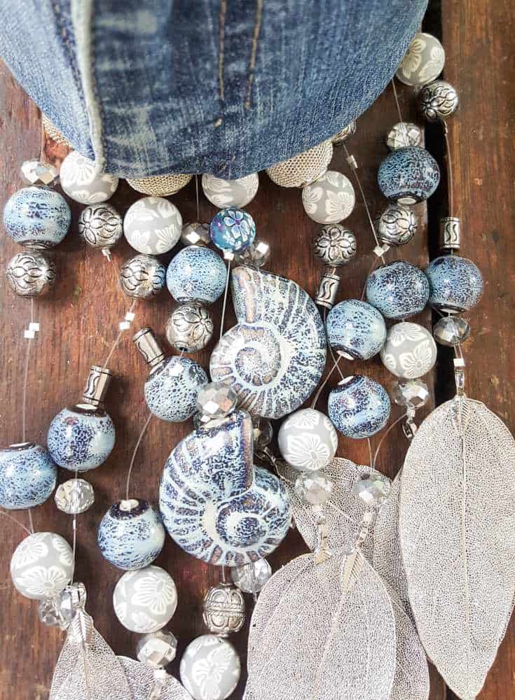 The different metals and types of beads will create a unique sound and the lengths add visual interest to the denim wind chime #DIYDenim #DenimIdeas #DenimMobile #DenimUpcycleIdeas #ACraftyMix #DenimUpcycle #DIYWindChime #TinCanRecycle #TinCanMobile #DenimWindChime