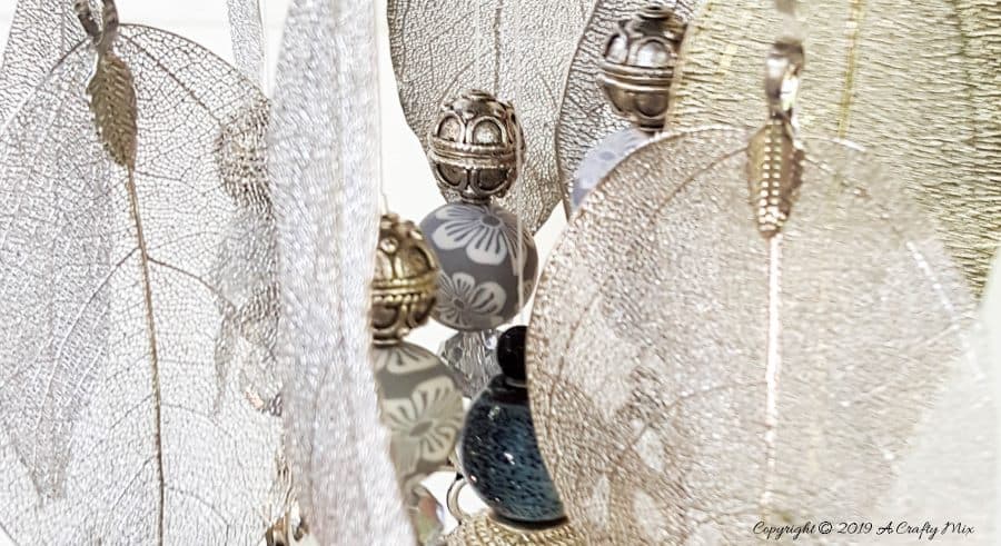 A close up of the delicate silver leaves and keys on the upcycled denim wind chime #DIYDenim #DenimIdeas #DenimMobile #DenimUpcycleIdeas #ACraftyMix #DenimUpcycle #DIYWindChime #TinCanRecycle #TinCanMobile #DenimWindChime