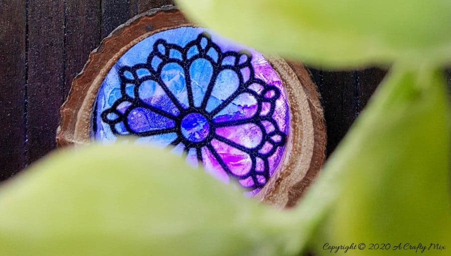 A close up of the stained glass window peaking through some plants #FairydoorDIY #FairyDoorIdeas #ACraftyMix #MakeAFairyDoor #MiniatureStainedGlass #AlcoholInk
