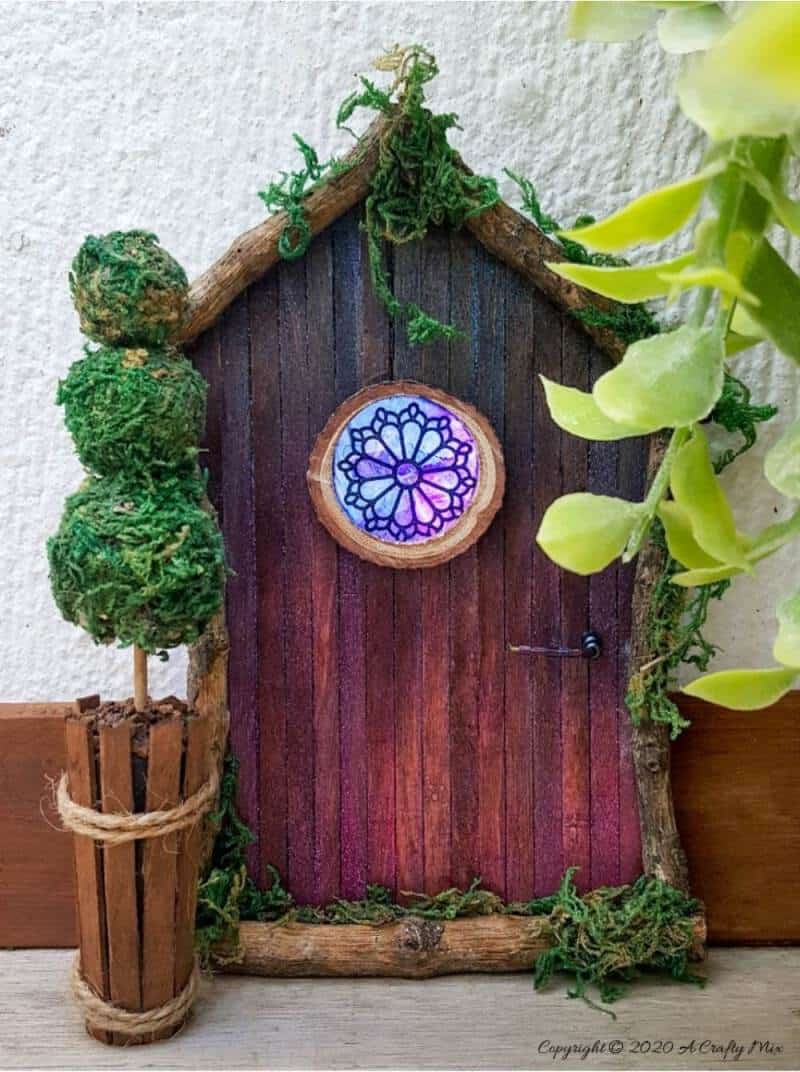 Welcome the fae folk into your home with this gorgeous stained glass fairy door. Made with things you probably already have in your craft cupboard, the door doubles up as a night light. #FairydoorDIY #FairyDoorIdeas #ACraftyMix #MakeAFairyDoor #MiniatureStainedGlass #AlcoholInk