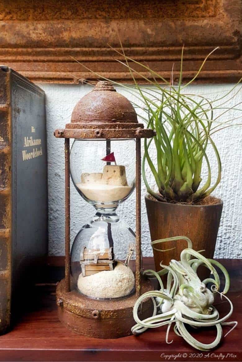Turn broken wine glasses into this unique Sands of Time hourglass. The tutorial includes how to make miniature sandcastles and a tiny treasure chest. #wineglassrepurpose #SandsofTime #uniquedecor #acraftymix #hourglassdecor