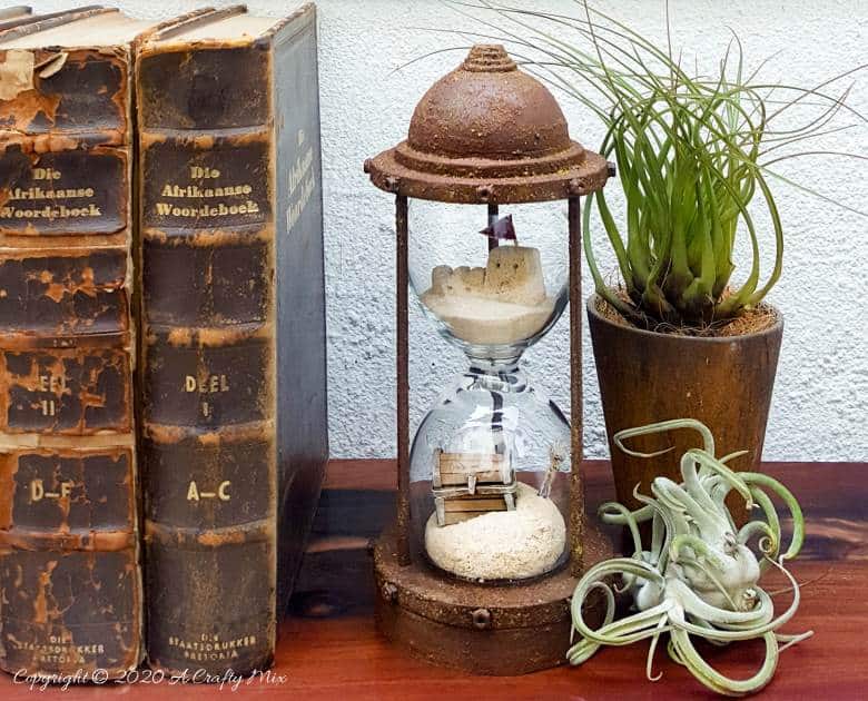 Turn broken wine glasses into this unique Sands of Time hourglass. The tutorial includes how to make miniature sandcastles and a tiny treasure chest. #wineglassrepurpose #SandsofTime #uniquedecor #acraftymix #hourglassdecor