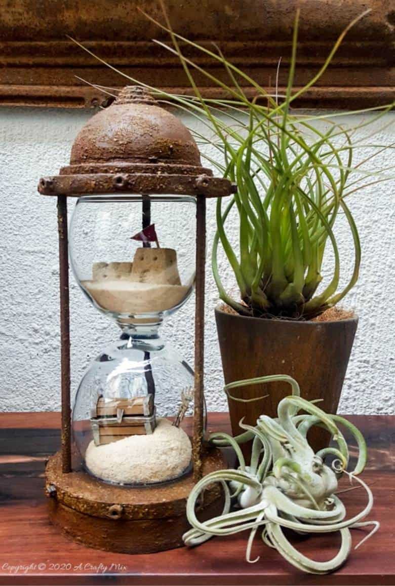 Turn broken wine glasses into this unique Sands of Time hourglass. The tutorial includes how to make miniature sandcastles and a tiny treasure chest. #wineglassrepurpose #SandsofTime #uniquedecor #acraftymix #hourglassdecor