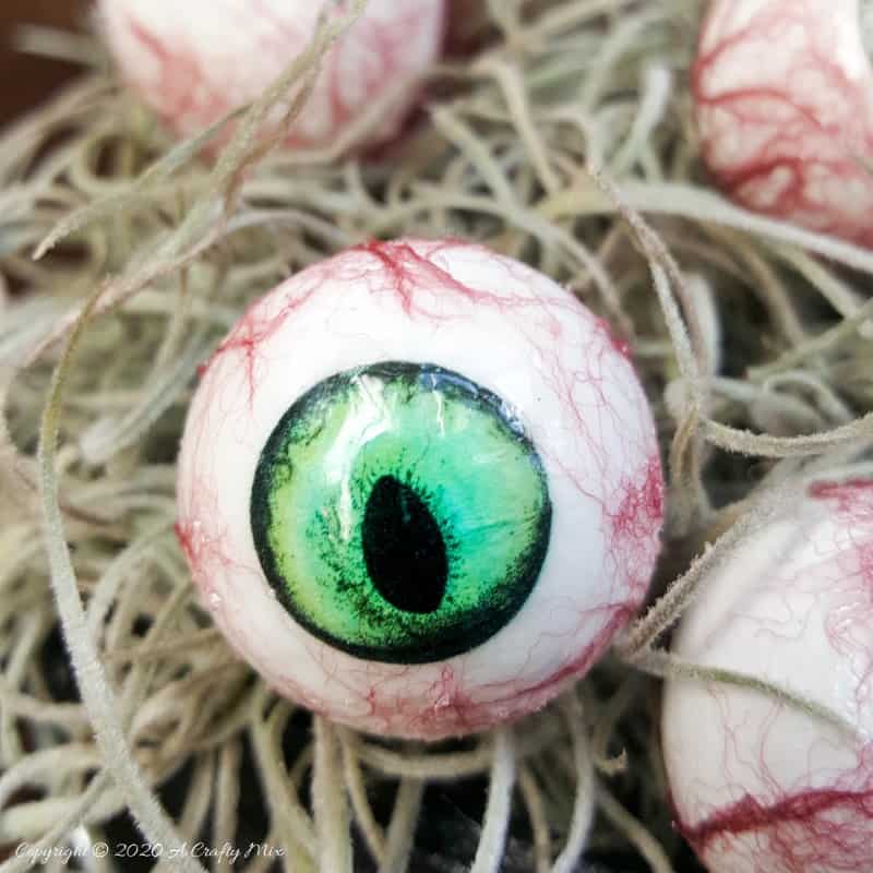 Up the creepy stakes this Halloween and make these realistic eyeballs. Quick and budget-friendly they'll add just the right spooky factor to your decor. The tutorial includes free "iris" printables to use #HalloweenDecor #CreepyEyeballs #ACraftyMix #FreePrintables