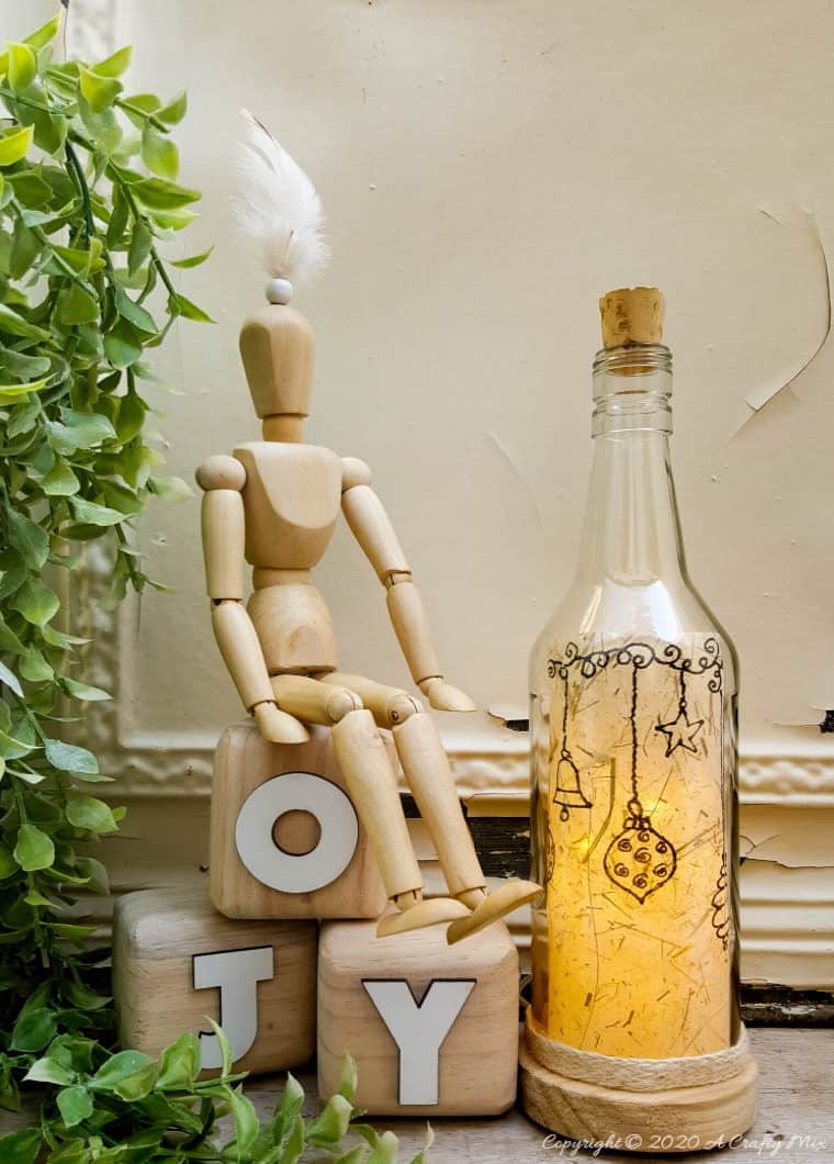 Take your glass bottle light to a whole new level with this DIY idea. A quick and easy way to repurpose and customize ONE bottle to fit any occasion or season with swappable art inserts. And you’ll have loads of fun coming up with new images to put inside too. #bottlelight #winebottlelights #acraftymix #bottlerepurpose #bottlecrafts