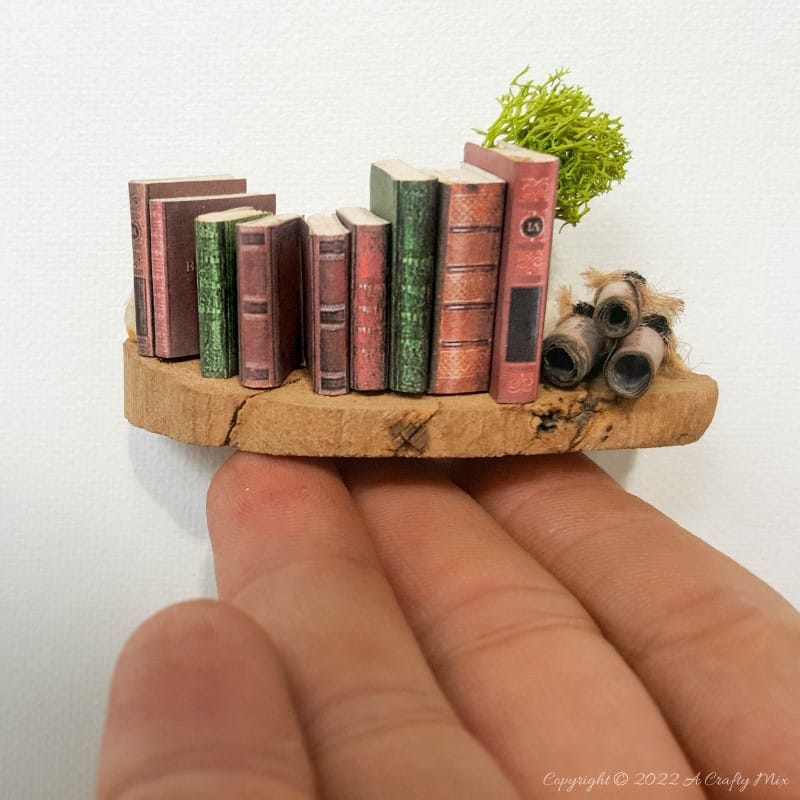A collection of small books, scrolls and topiary on the floating shelf. Get the tutorial @ A Crafty Mix