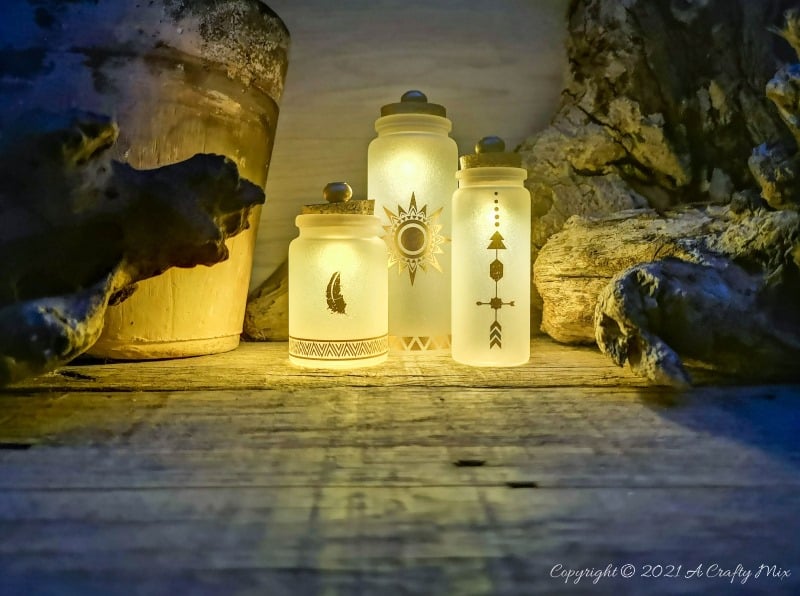 A perfect beginner-friendly home decor project that only takes a few minutes to make! These gorgeous glass bottle lights with gold accents look lovely no matter where you display them. Place them on your mantle or bookshelf or use them as a centerpiece at a special event or bridal shower. #DIYBottleDecor #ACraftyMix #GlassBottleIdeas