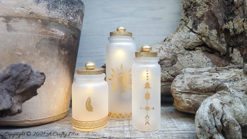 A perfect beginner-friendly home decor project that only takes a few minutes to make! These gorgeous glass bottle lights with gold accents look lovely no matter where you display them. Place them on your mantle or bookshelf or use them as a centerpiece at a special event or bridal shower. #DIYBottleDecor #ACraftyMix #GlassBottleIdeas