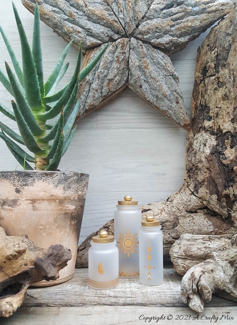 A perfect beginner-friendly home decor project that only takes a few minutes to make! These gorgeous glass bottle lights with gold accents look lovely no matter where you display them. Place them on your mantle or bookshelf or use them as a centerpiece at a special event or bridal shower. #DIYBottleDecor #ACraftyMix #GlassBottleIdeas