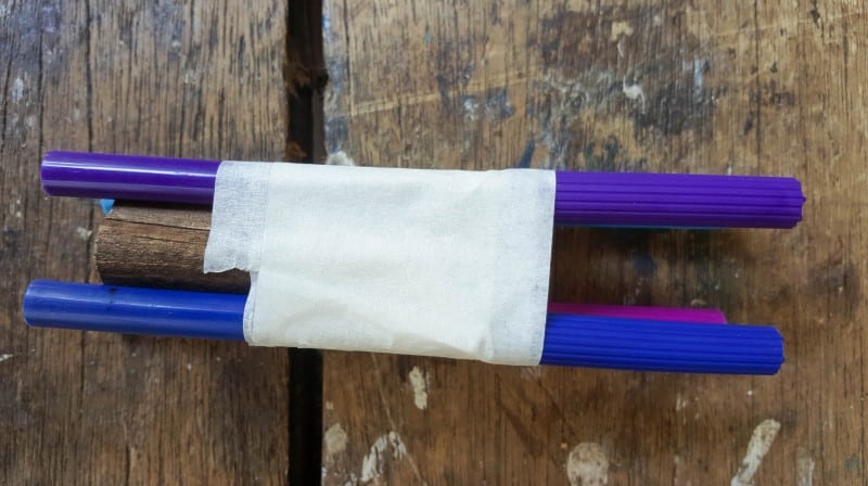 Tape the pens to the piece of wood