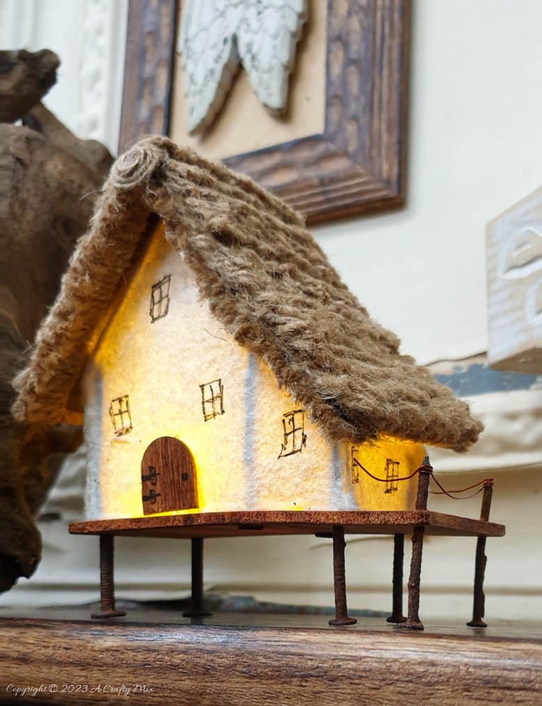 This paper house with a miniature thatch roof is made entirely from scraps and recycled materials, giving it a creative, whimsical feel. The lights add a little magic, and we all need more of that in our lives. In this step-by-step tutorial, we&rsquo;ll show you how you can make your own and share an easy way to thatch a small roof. #ACraftyMix