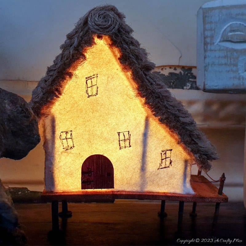 This paper house with a miniature thatch roof is made entirely from scraps and recycled materials, giving it a creative, whimsical feel. The lights add a little magic, and we all need more of that in our lives. In this step-by-step tutorial, we&rsquo;ll show you how you can make your own and share an easy way to thatch a small roof. #ACraftyMix
