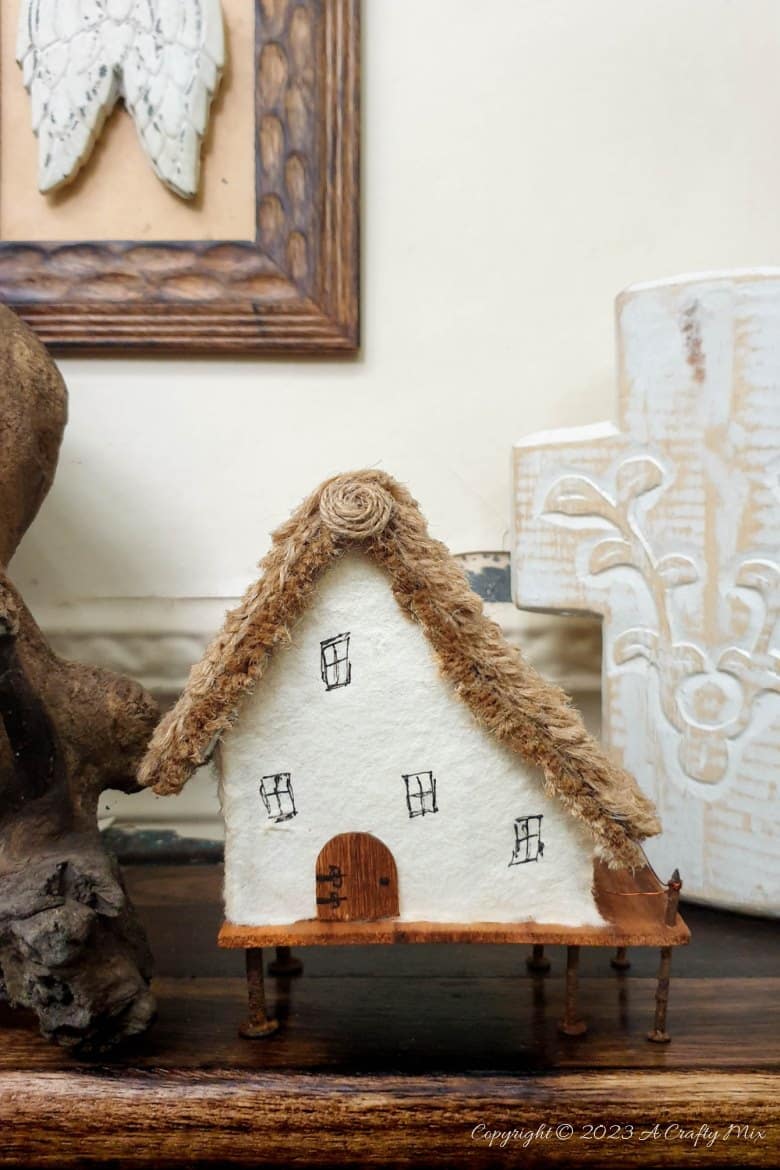 This paper house with a miniature thatch roof is made entirely from scraps and recycled materials, giving it a creative, whimsical feel. The lights add a little magic, and we all need more of that in our lives. In this step-by-step tutorial, we&rsquo;ll show you how you can make your own and share an easy way to thatch a small roof. #ACraftyMix
