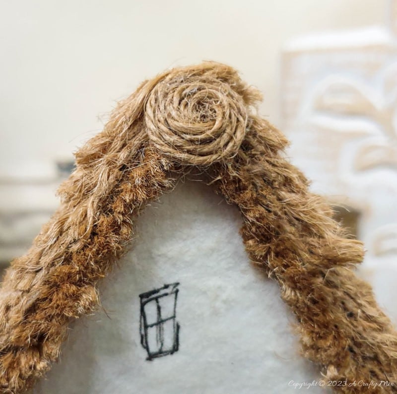 This paper house with a miniature thatch roof is made entirely from scraps and recycled materials, giving it a creative, whimsical feel. The lights add a little magic, and we all need more of that in our lives. In this step-by-step tutorial, we&rsquo;ll show you how you can make your own and share an easy way to thatch a small roof. #ACraftyMix