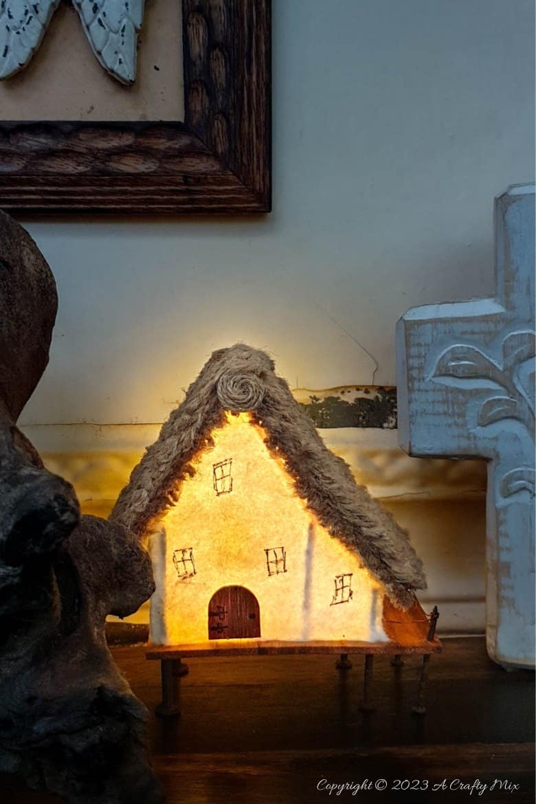 This paper house with a miniature thatch roof is made entirely from scraps and recycled materials, giving it a creative, whimsical feel. The lights add a little magic, and we all need more of that in our lives. In this step-by-step tutorial, we&rsquo;ll show you how you can make your own and share an easy way to thatch a small roof. #ACraftyMix