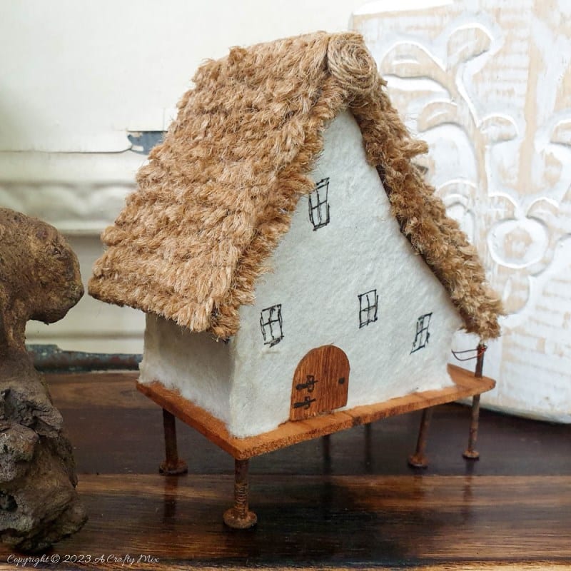 This paper house with a miniature thatch roof is made entirely from scraps and recycled materials, giving it a creative, whimsical feel. The lights add a little magic, and we all need more of that in our lives. In this step-by-step tutorial, we&rsquo;ll show you how you can make your own and share an easy way to thatch a small roof. #ACraftyMix