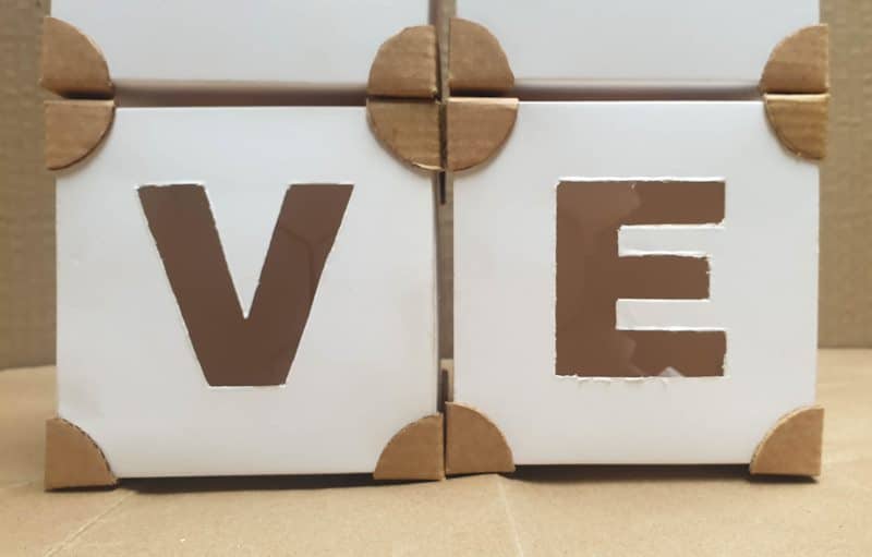 Small decorative cardboard boxes that have been decorated with corners and letter cut-outs.