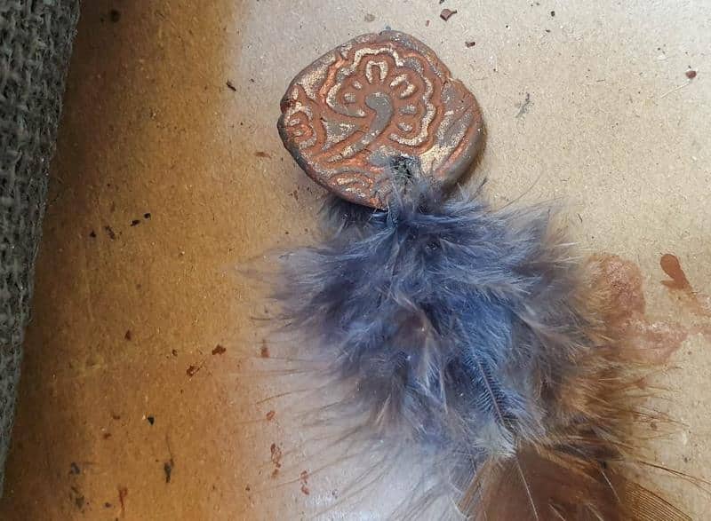 A feather and handmade clay token to decorate the paintbrush holder