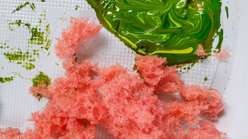 Chunks of ripped sponge and green paint mixed in a bowl
