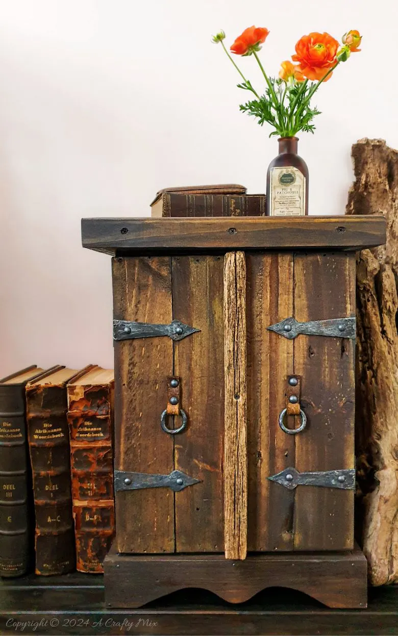 Repurpose a crate to make a rustic side table and give your space a unique, creative makeover. This DIY project is a perfect way to add a touch of vintage charm to your home and create extra storage at the same time. The free tutorial will guide you through the whole process. As an added bonus, we’ll show you how to make faux metal hinges using cardboard and create custom door pulls.