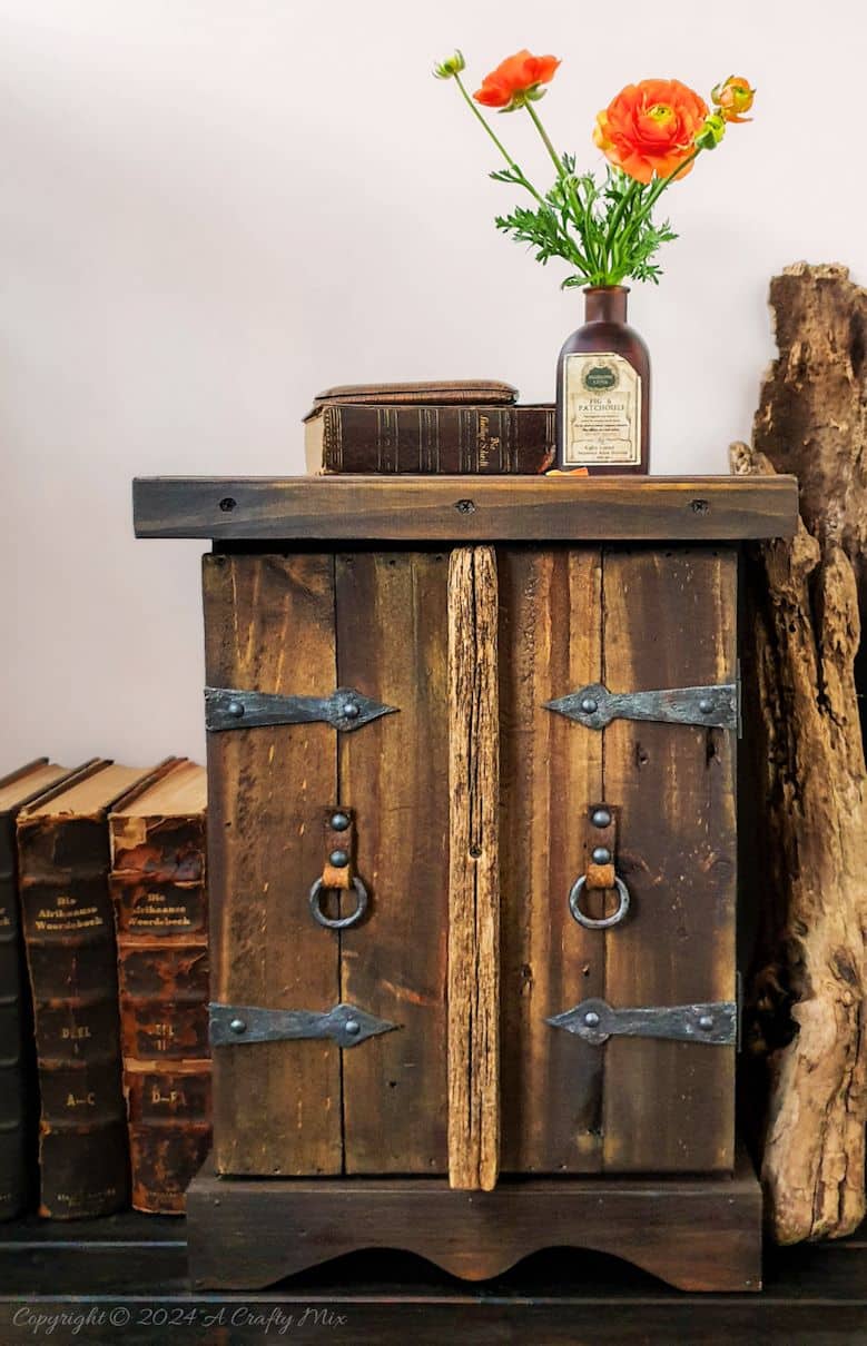 Repurpose a crate to make a rustic side table and give your space a unique, creative makeover. This DIY project is a perfect way to add a touch of vintage charm to your home and create extra storage at the same time. The free tutorial will guide you through the whole process. As an added bonus, we’ll show you how to make faux metal hinges using cardboard and create custom door pulls.