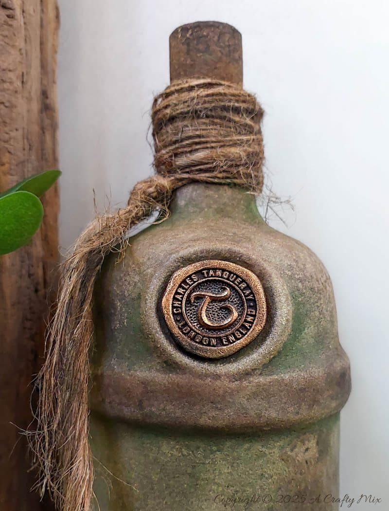 Upcycle ordinary bottles into old world treasures with this easy DIY. This beginner-friendly tutorial teaches you how to create an authentic antique clay finish using simple powdered food coloring and texture paste. Perfect for rustic or old-world d&eacute;cor.