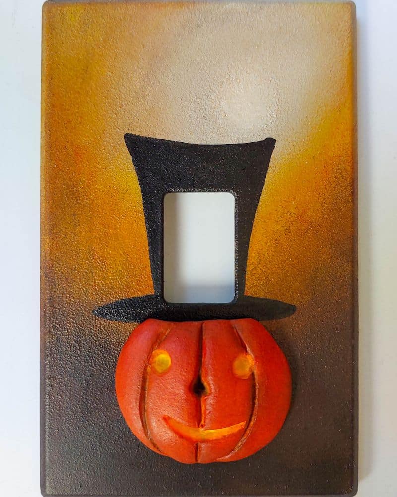 Looking for a creative way to dress up your d&eacute;cor for the spooky season? This DIY Halloween light switch cover features a cheerful pumpkin with a tall black top hat, set in a beautifully ornate frame. Simple to make and perfect for living rooms, entryways, or party spaces, this beginner-friendly craft transforms an ordinary switch plate into playful, functional art.