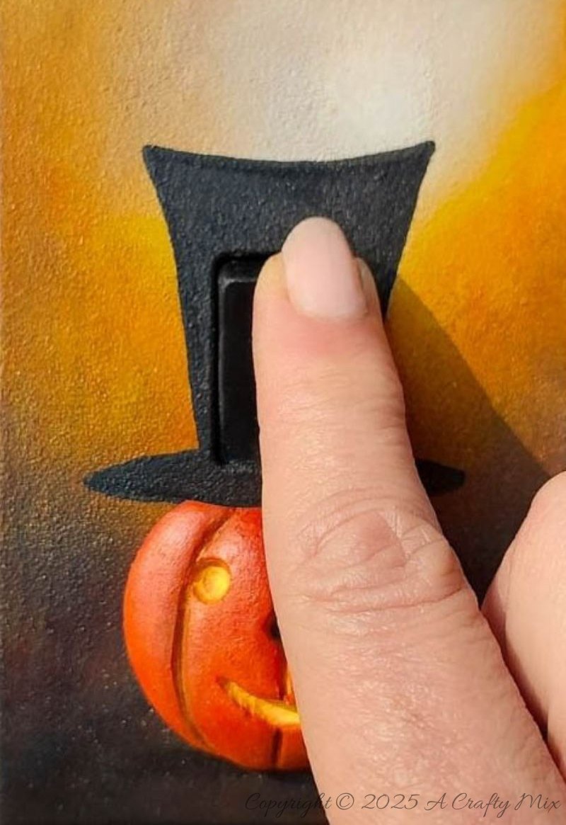 Looking for a creative way to dress up your d&eacute;cor for the spooky season? This DIY Halloween light switch cover features a cheerful pumpkin with a tall black top hat, set in a beautifully ornate frame. Simple to make and perfect for living rooms, entryways, or party spaces, this beginner-friendly craft transforms an ordinary switch plate into playful, functional art.