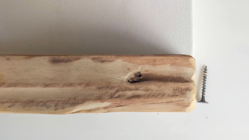 A piece of wood lies underneath an empty canvas and there is a wood screw on the side.
