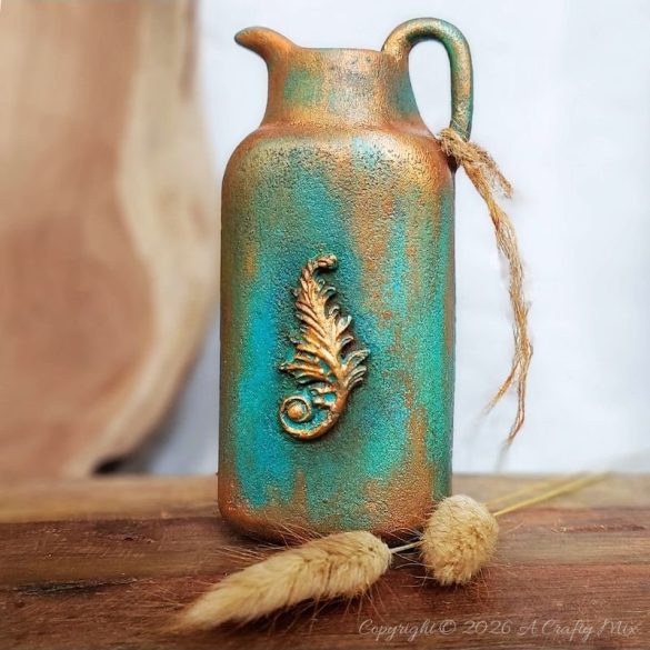 Upcycled plastic baby powder bottle transformed into a tall jug‑shaped vase with copper and turquoise patina finish, styled with dried bunny tail grass on a wooden surface.