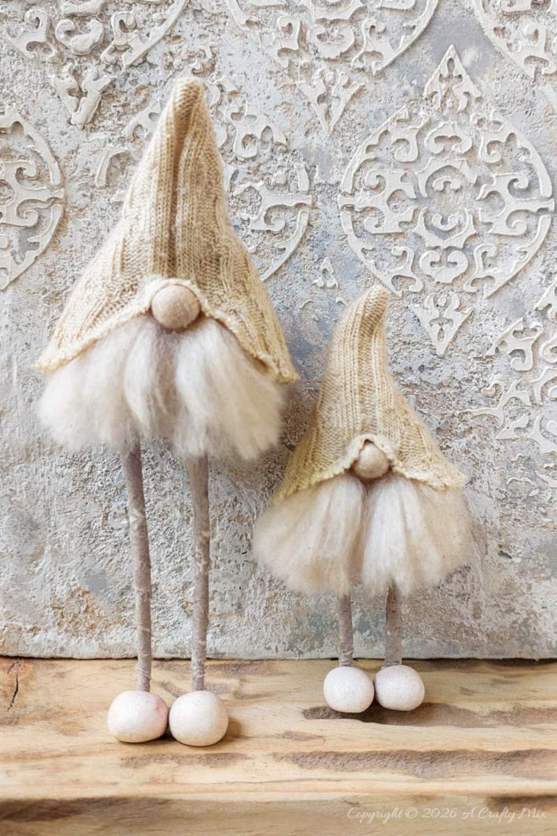 Two small Scandinavian gnomes stand on a floating shelf with a texture canvas in the background