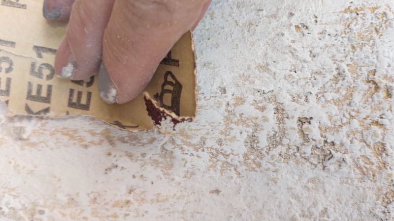 A hand holding sandpaper with a texture canvas in the background