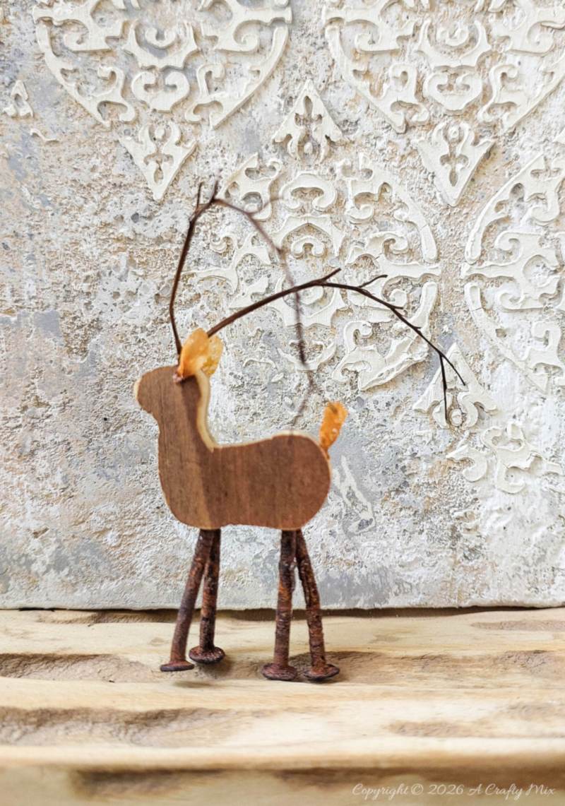 A small reindeer standing on a shelf in front of a textured canvas
