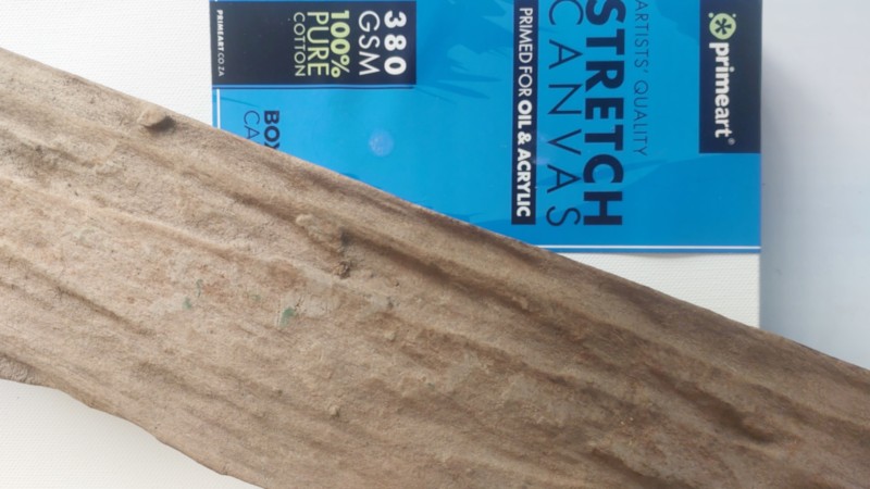 A weathered piece of wood lies on top of a box canvas
