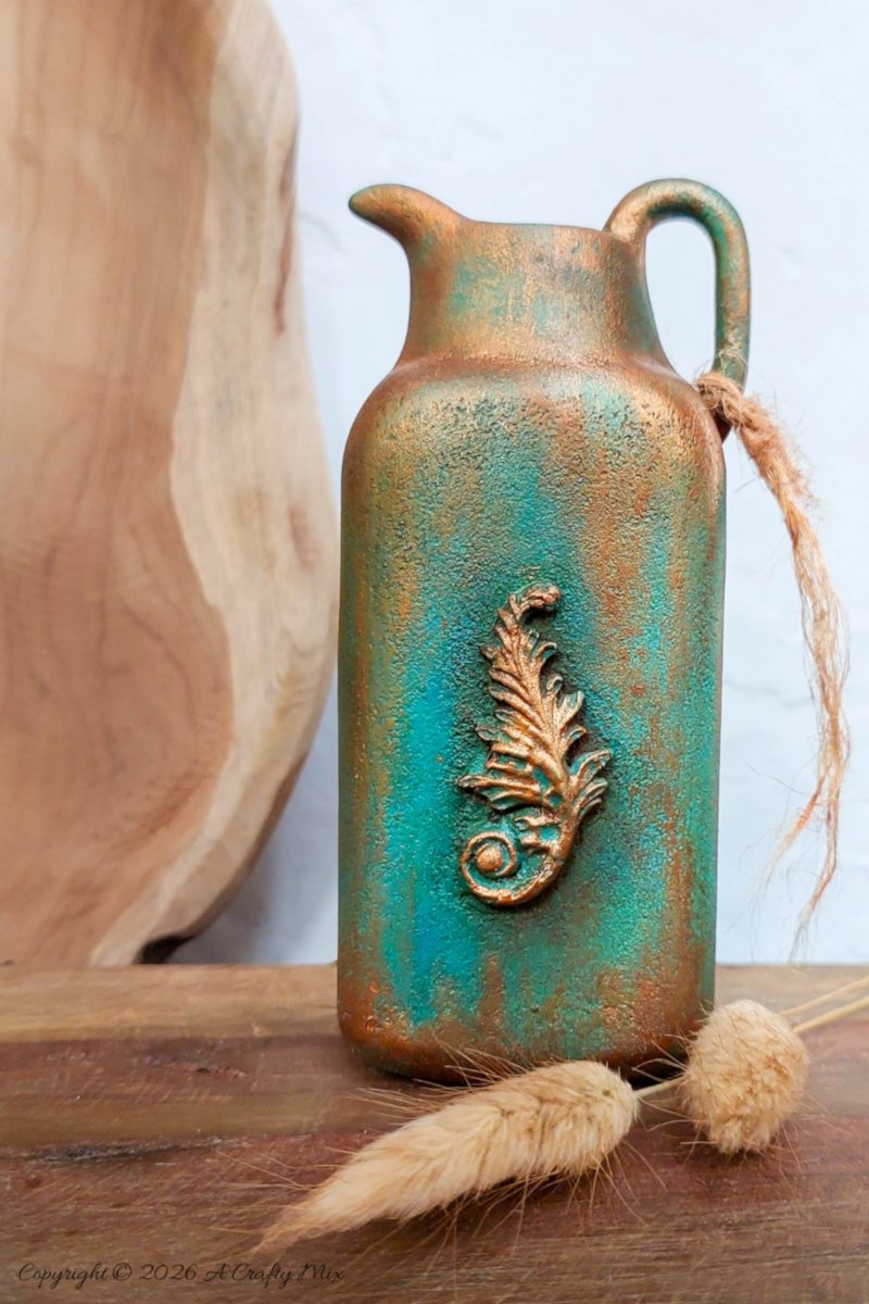 Upcycled plastic baby powder bottle transformed into a tall jug‑shaped vase with copper and turquoise patina finish, styled with dried bunny tail grass on a wooden surface.