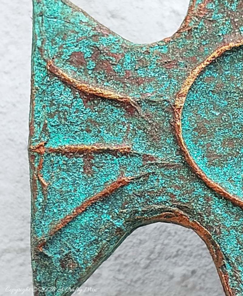 A close up of the tail of a patinaed fish used as DIY coastal decor, crafted from layered cardboard and copper tape.