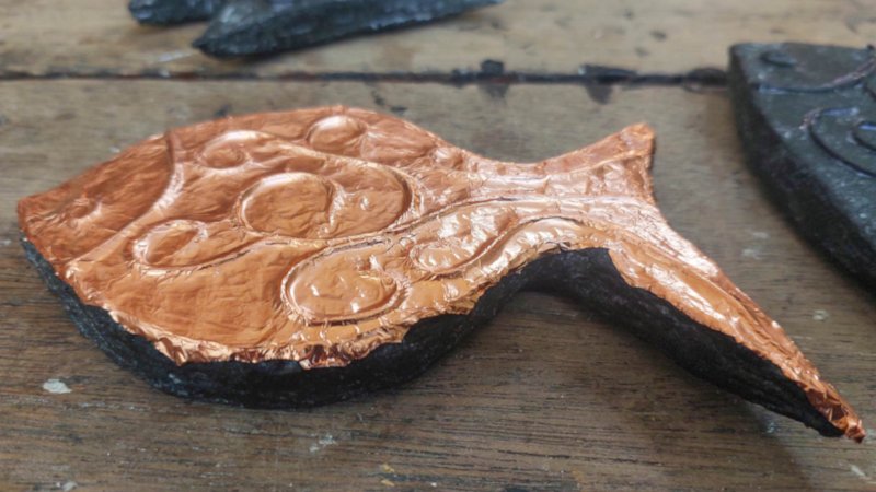 A copper fish made from cardboard lies on a wood surface