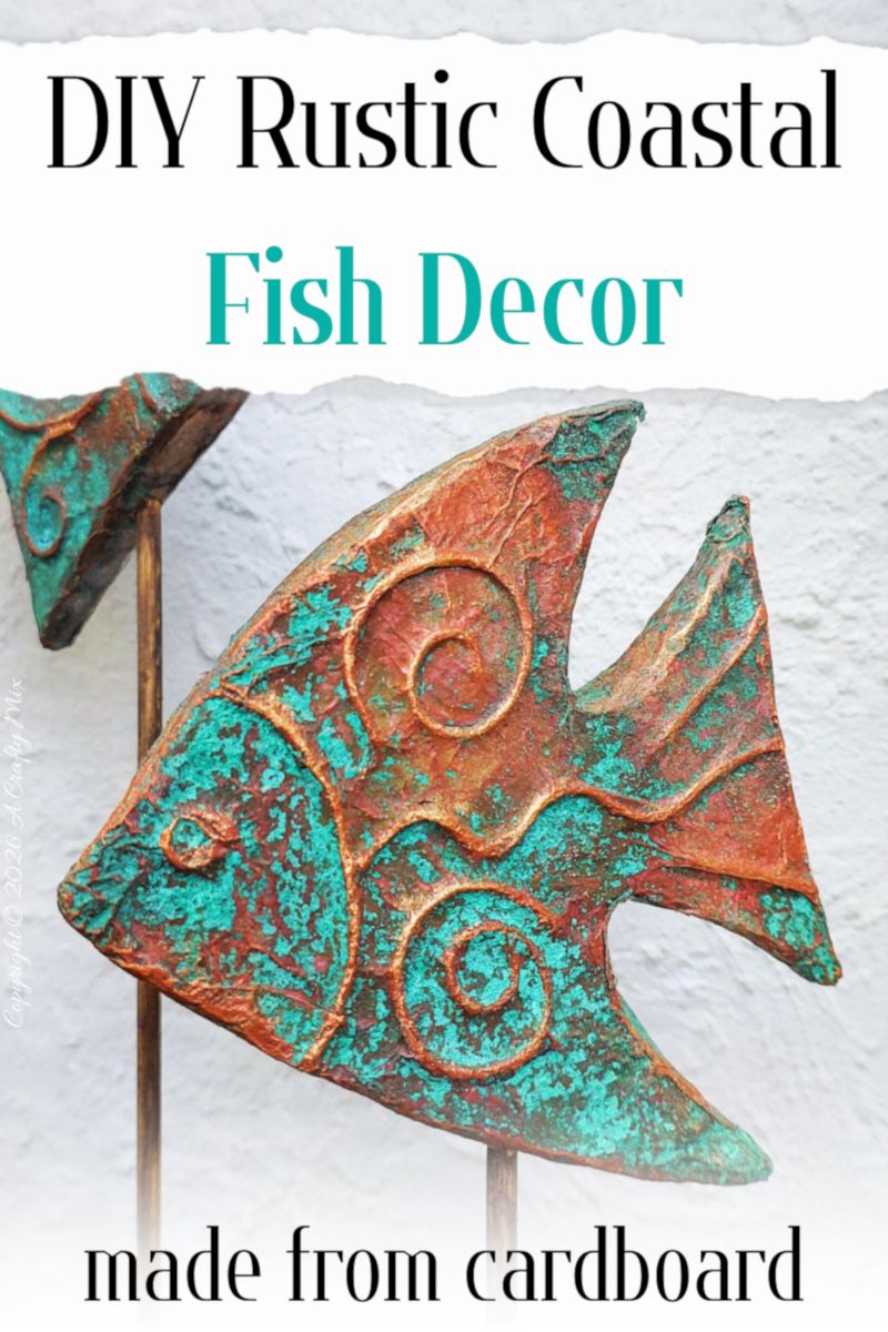 Two rustic patina fish on wooden sticks used as DIY coastal decor, crafted from layered cardboard and copper tape.