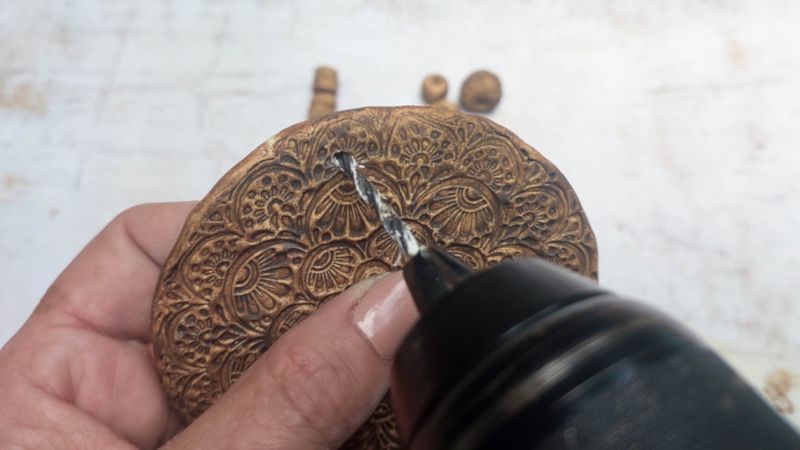 Close up showing a hand drilling holes into the bottom of a clay medallion