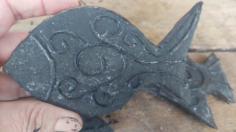 A hand holding a cardboard fish that has been painted black and decorated with cord