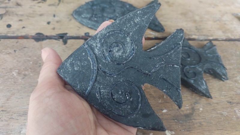 A hand holding a cardboard fish that has been painted black and decorated with cord