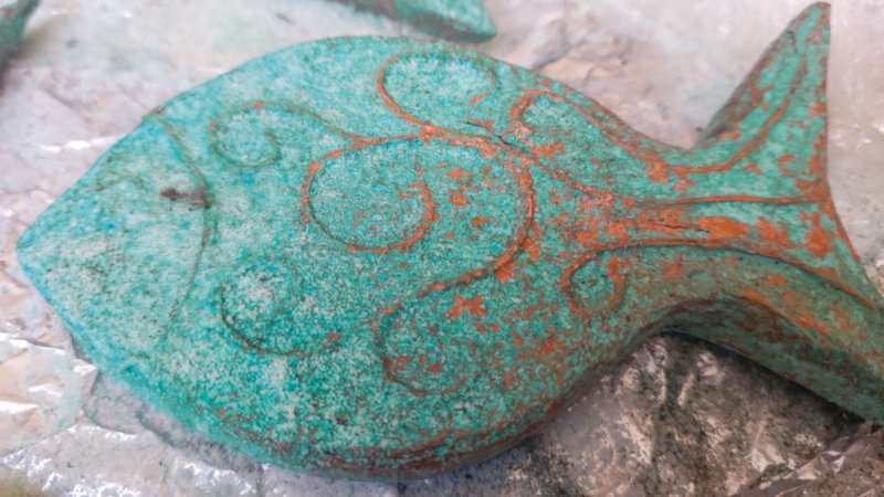 A rustic patina fish lying on a wooden surface before being used as DIY coastal decor