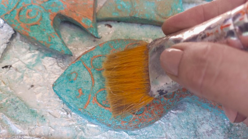 A process shot of a hand using a paintbrush to remove salt crystals from a copper patina fish