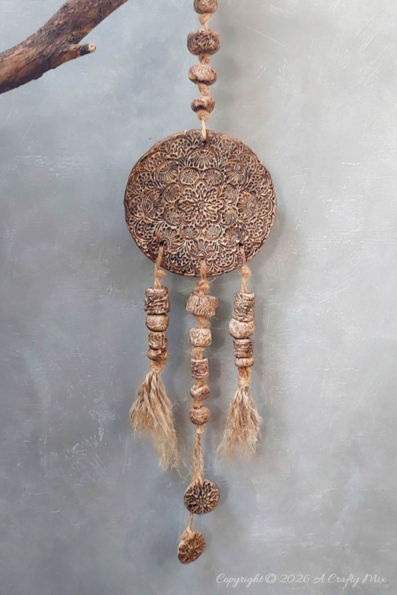 A rustic, b oho clay medallion with bead detail hanging against a wall.